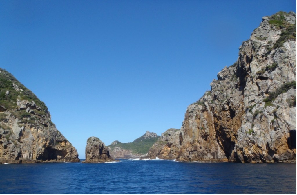 Personal photograph of part of the Poor Knights Islands in New Zealand. Rocky cliff faces, se and sky.